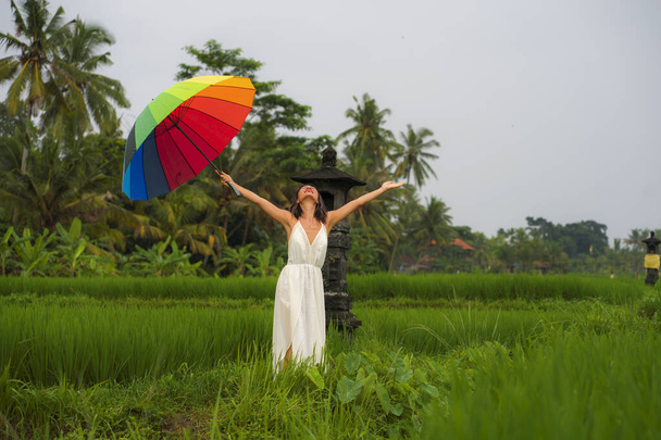 outdoors holidays portrait of young happy and beautiful Asian Korean woman in white dress and rainbow umbrella enjoying nature carefree at tropical green field walking around  - Fotoğraf, Görsel