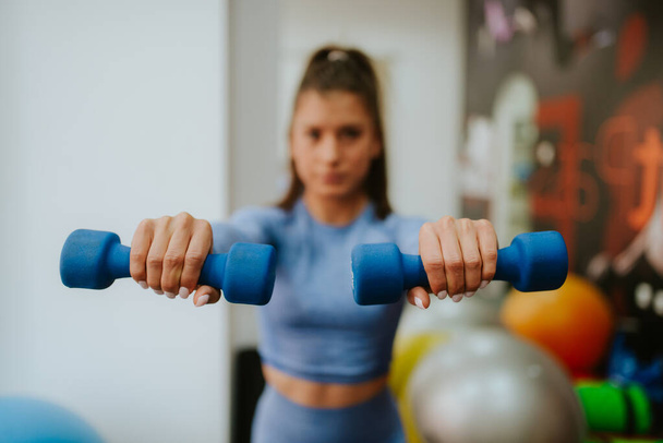 A young beautiful caucasian woman in blue sports equipment exercises in the gym with weights - Foto, Imagem