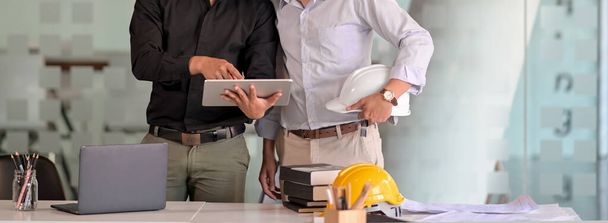 Zdjęcie dwóch inżynierów współpracujących z tabletem cyfrowym, laptopem i sprzętem biurowym w sali konferencyjnej  - Zdjęcie, obraz