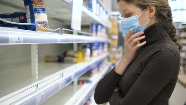 Panik-Coronovirus. Traurige Frau mit Maske steht vor leerem Regal im Supermarkt - Filmmaterial, Video
