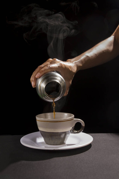 hand serving or pouring hot coffee into a cup in black background - Foto, Imagen