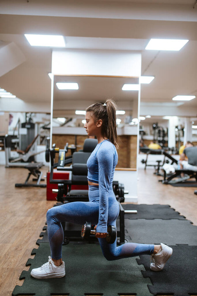 Eine junge schöne Frau in blauen Sportgeräten trainiert im Fitnessstudio mit Gewichten - Foto, Bild