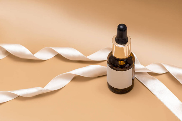 Serum, essential oils or fluid collagen in brown glass bottle with pipette, isolated on brown backgraund with beige ribbon, empty label, copyspace - Φωτογραφία, εικόνα