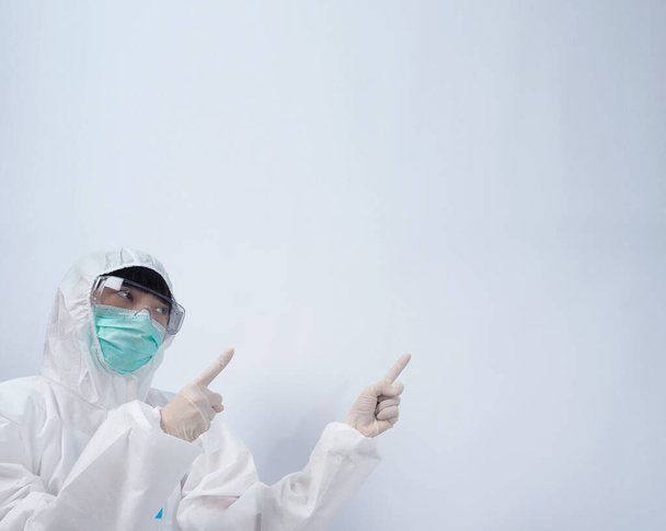 Doctor in PPE suit or Personal Protection Equipment point out to copy space and wearing white color medical rubber gloves and clear goggles glasses and green N95 mask to protect and fight pandemic virus - Photo, Image