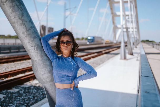 Portrait of a young caucasian beautiful girl in blue sports equipment on the bridge - Photo, Image