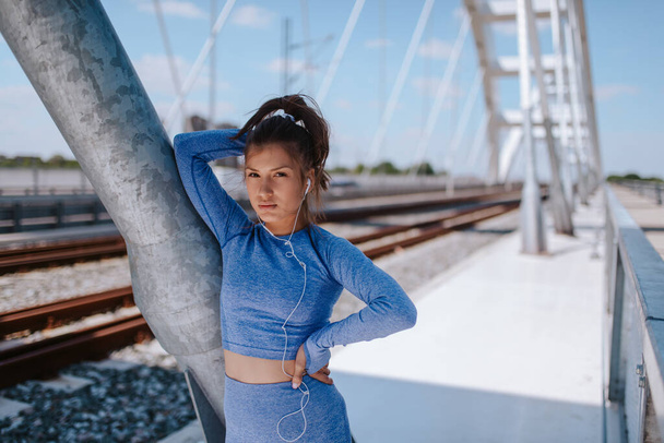 Portret młodej białej pięknej dziewczyny w niebieskim sprzęcie sportowym na moście - Zdjęcie, obraz