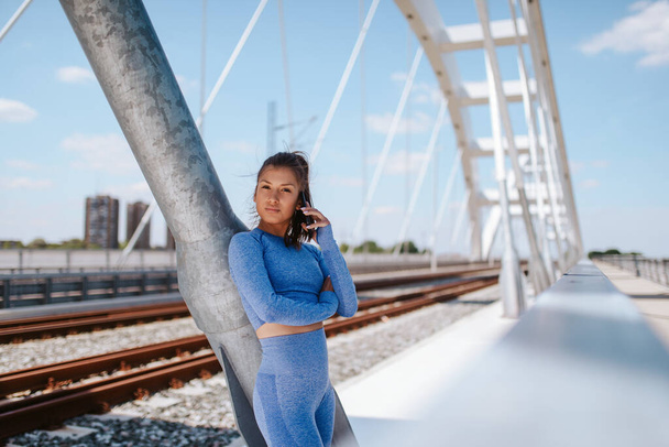 Portrait of a young caucasian beautiful girl in blue sports equipment on the bridge - Photo, Image