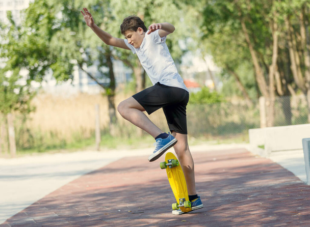 Adolescente em camiseta branca passa tempo livre treinando patinação no parque da cidade. Bonito menino agradável gosta de dia ao ar livre com skate. Hobby, esporte para crianças. - Foto, Imagem