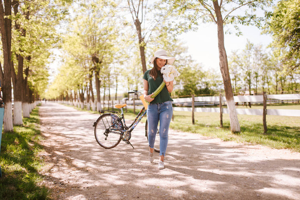 In het park staat een mooie jonge vrouw met strohoed, fiets en bloemen. Leven in een dorp - Foto, afbeelding