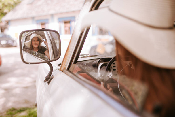 Μια όμορφη νεαρή λευκή γυναίκα με ψάθινο καπέλο στον πίσω καθρέφτη ενός φορτηγού. - Φωτογραφία, εικόνα