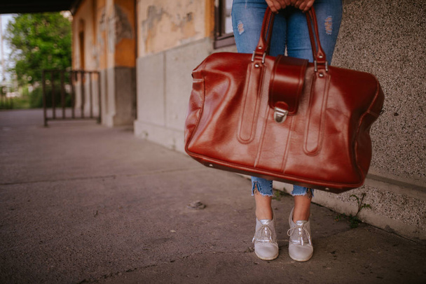 Primer plano de una maleta marrón en manos de una joven mujer caucásica en la estación de tren
 - Foto, Imagen