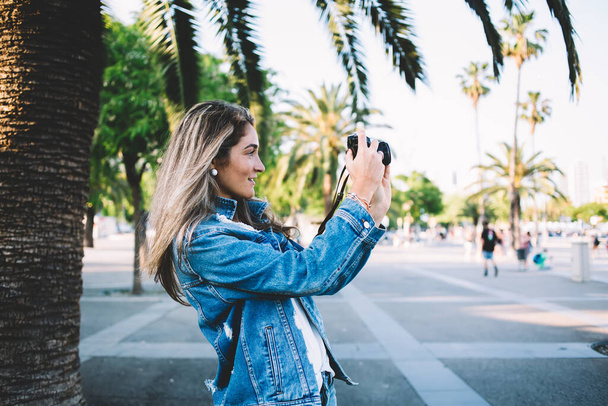 Side näkymä houkutteleva naispuolinen turisti ottaa kuvia modernin teknologian kevään aikana lomat Barcelonassa, tyylikäs hipster tyttö farkut vaatteet keskittyen kamera valokuvaus maisema - Valokuva, kuva