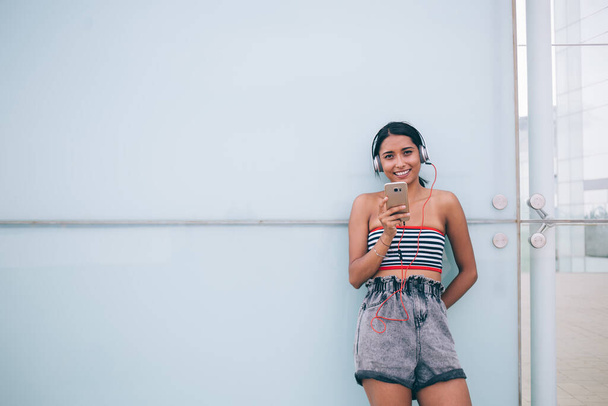 Portrait of pretty cheerful hipster girl spending leisure in city enjoying sound playlist with popular track connected to 4g wireless on smartphone gadget for listening electronic audio records - Photo, Image