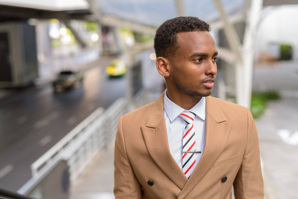 Junge gutaussehende afrikanische Geschäftsleute denken, während sie die Rolltreppe in der Stadt hinaufsteigen - Foto, Bild