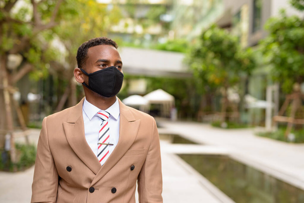 Young African businessman thinking with mask for protection from corona virus outbreak in the city with nature - Fotoğraf, Görsel