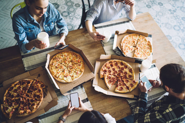 From above tasty fresh appetizing pizza in boxes on table for crop hungry friends sitting around and browsing mobile phone  - Zdjęcie, obraz