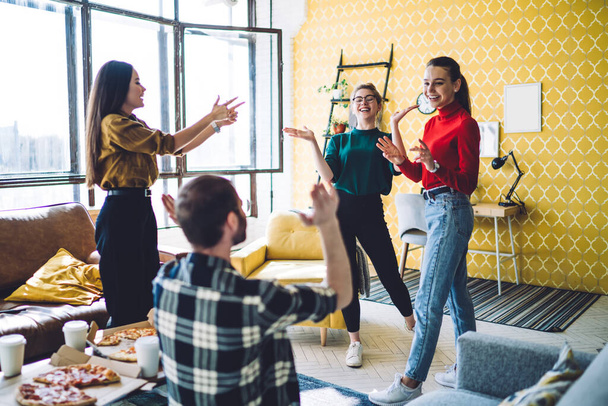 Cheerful people in casual outfit speaking and gesturing while standing by table with pizza boxes and takeaway cups in modern apartment - Фото, изображение