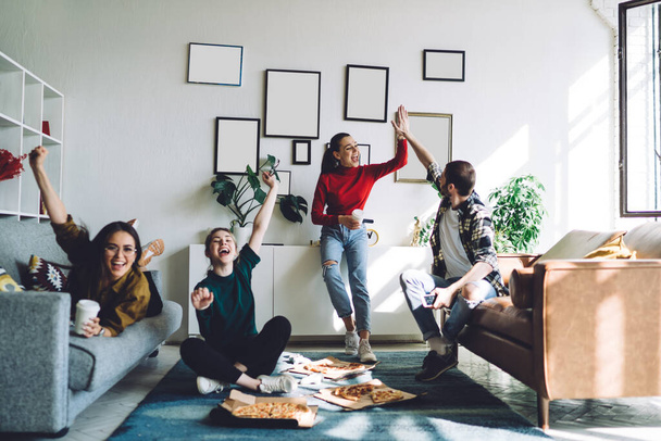 Happy optimistic satisfied young people celebrating success during watching sport match on TV with high five gesture and raised arms while eating pizza - Foto, Bild