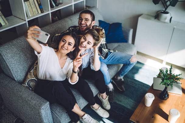 From above young happy cheerful stylish trendy students in cozy modern design living room sitting at comfortable couch and taking selfie - Valokuva, kuva
