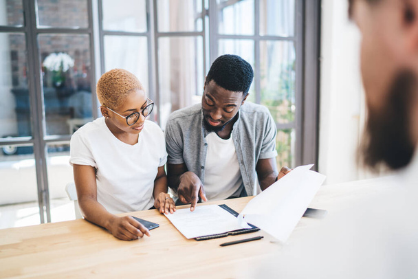 Thoughtful African American couple sitting at table in apartment in front of realtor reading estate contract with attention and talking - Фото, зображення