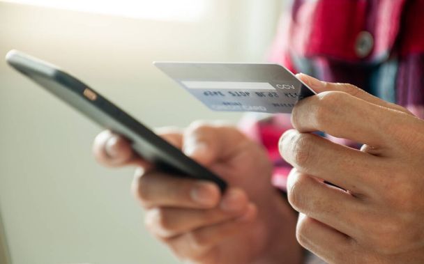 Τα αρσενικά χέρια χρησιμοποιούν πιστωτικές κάρτες για online αγορές μέσω έξυπνων τηλεφώνων. Πληρωμή για προϊόντα σε απευθείας σύνδεση - Φωτογραφία, εικόνα