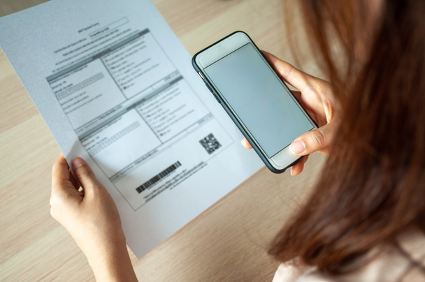 Женщина использует смартфон для сканирования штрих-кода, чтобы оплачивать ежемесячные телефонные счета после получения счета, отправленного домой. Концепция оплаты счетов онлайн - Фото, изображение