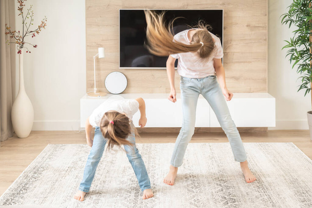 Две сестры весело танцуют в гостиной, счастливая семейная концепция
 - Фото, изображение