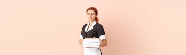 Beautiful young chambermaid with towels and space for text on color background - Photo, Image