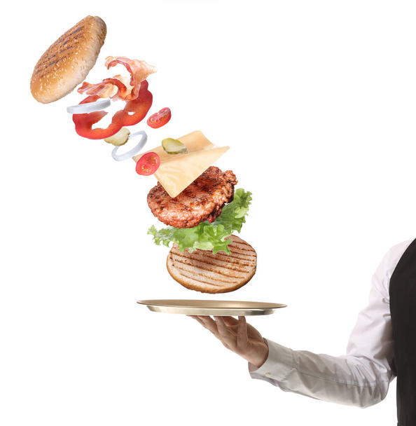 Waiter holding tray with flying ingredients of burger on white background - Photo, Image