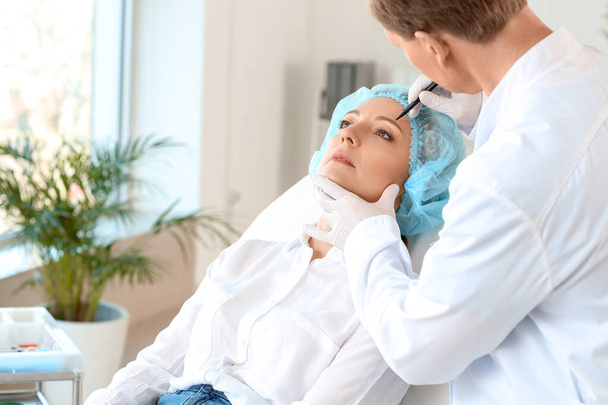 Plastisch chirurg brengt littekens aan op het gezicht van de vrouw in de kliniek - Foto, afbeelding