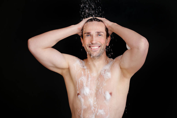 Handsome man taking shower on dark background - Фото, зображення
