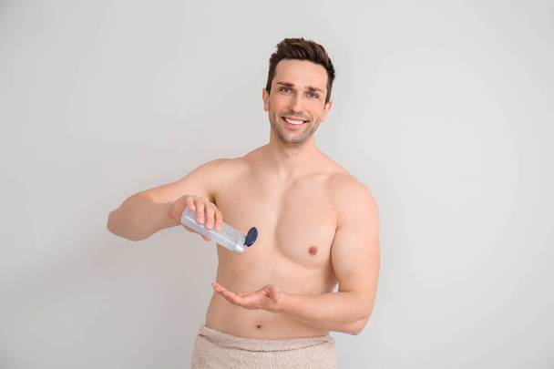 Schöner Mann mit Duschgel auf hellem Hintergrund - Foto, Bild