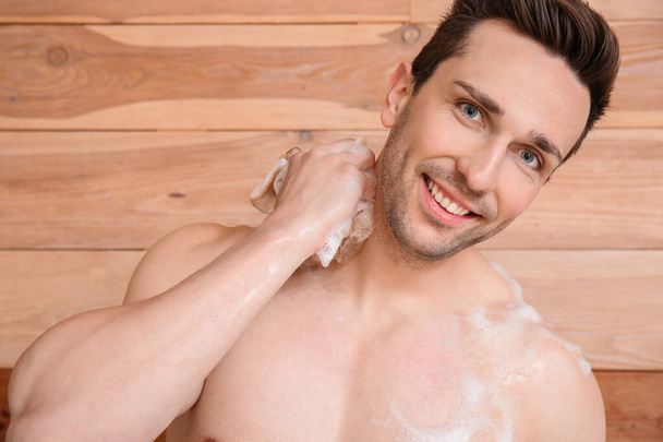 Hombre guapo tomando ducha sobre fondo de madera
 - Foto, imagen