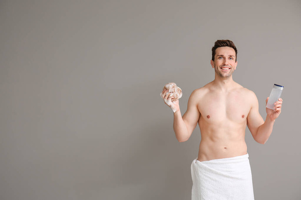 Hombre guapo con gel de ducha y esponja sobre fondo gris
 - Foto, Imagen