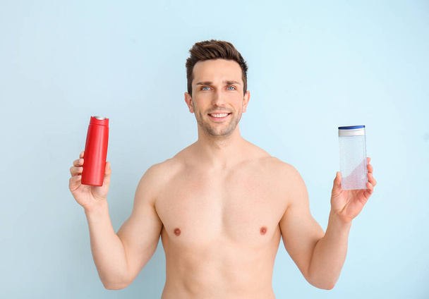 Handsome man with shower gels on color background - Φωτογραφία, εικόνα