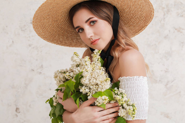 Beautiful young woman with bouquet of lilac flowers on light background - Photo, Image