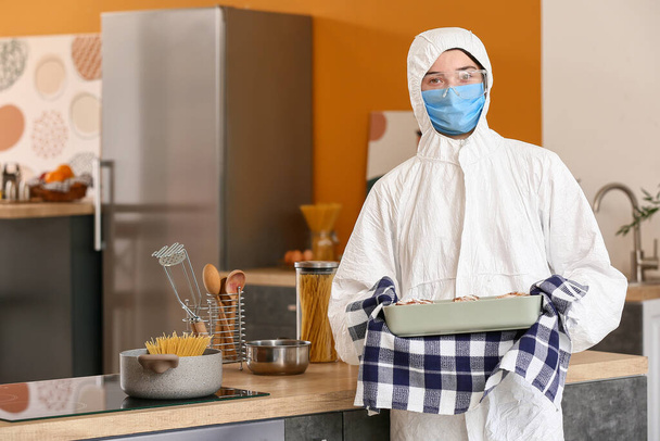 Mutfakta biyolojik tehlike kıyafeti giymiş bir kadın yemek pişiriyor. - Fotoğraf, Görsel
