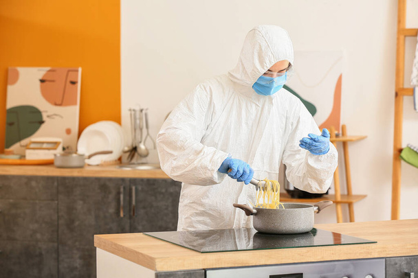 Woman in biohazard suit cooking in kitchen - Foto, Bild
