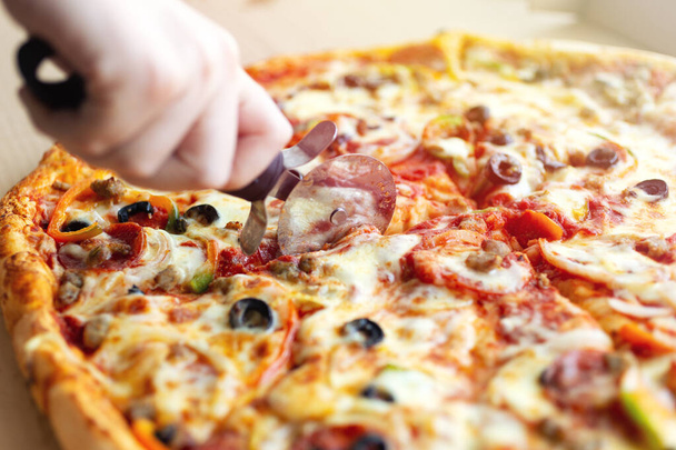 Close-up van de hand snijden grote cheesy pepperoni pizza, achtergrond macro - Foto, afbeelding