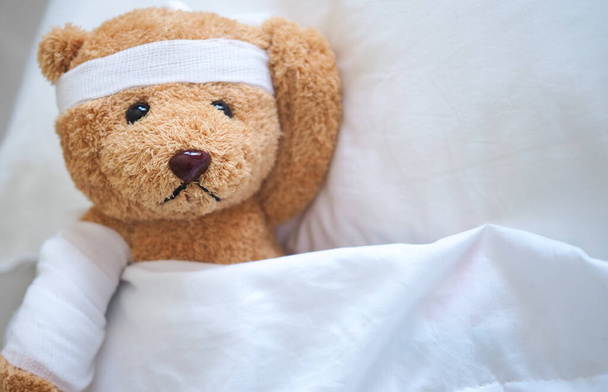 Teddy maci feküdt betegen az ágyban egy fejpánt és egy ruha fedett - Fotó, kép