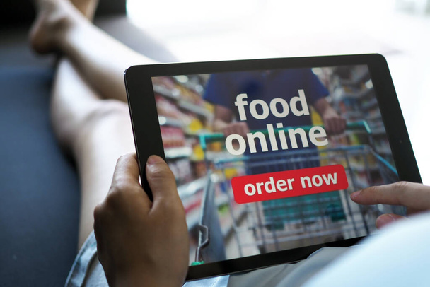 Le donne usano compresse per ordinare cibo online mentre sono sdraiate sul divano a casa. - Foto, immagini