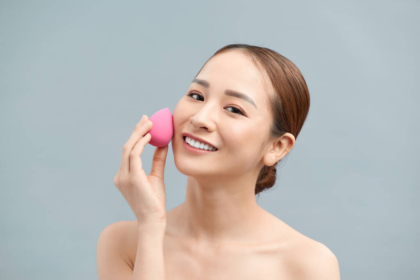 Hermosa mujer joven aplicando maquillaje usando esponja de licuadora de belleza
. - Foto, imagen