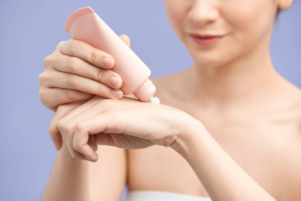 Šťastná žena hydratační ruce kůže s hydratační krém na fialovém pozadí - Fotografie, Obrázek