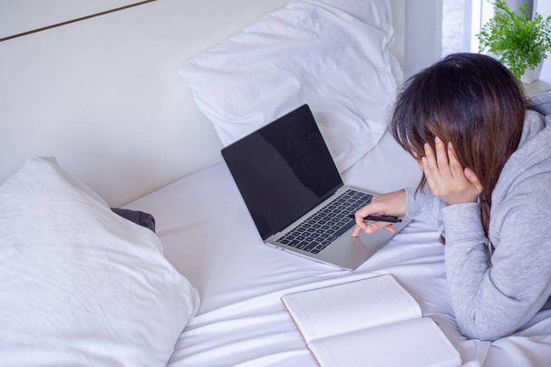 Студентка учится и делает домашнее задание через блокнот в кровати. Изучение в Интернете дома - это способ уменьшить распространение вируса, который легко инфицируется в обществе. Концептуальное исследование онлайн
. - Фото, изображение