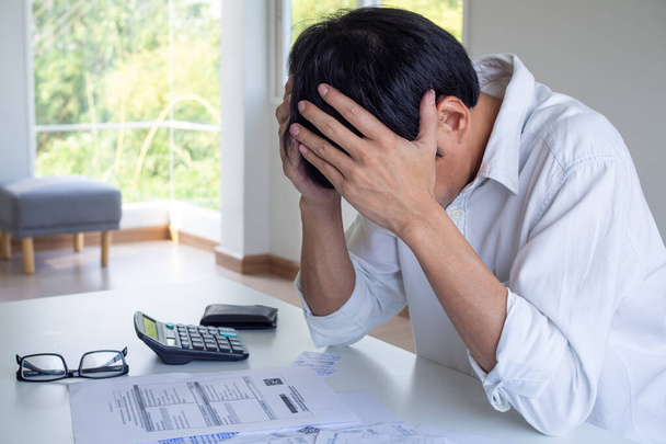 Muž sedí ve stresu kvůli dluhu, který je čas splatit. Znepokojení kvůli měsíčnímu vyúčtování výdajů na stole. - Fotografie, Obrázek
