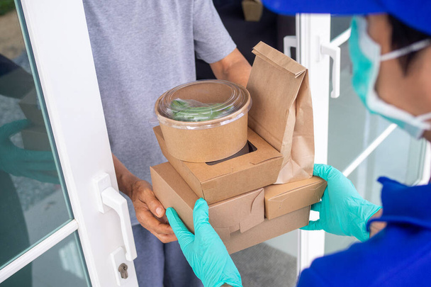 The shipper wears a mask and gloves, delivering food to the home of the online buyer. stay at home reduce the spread of the covid-19 virus. The sender has a service to deliver products or food quickly - Photo, image