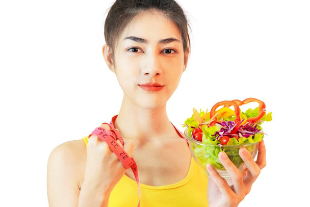 Jonge mooie aziatische vrouw droeg geel ondershirt, Holding een salade glazen beker geïsoleerd op witte achtergrond - Foto, afbeelding