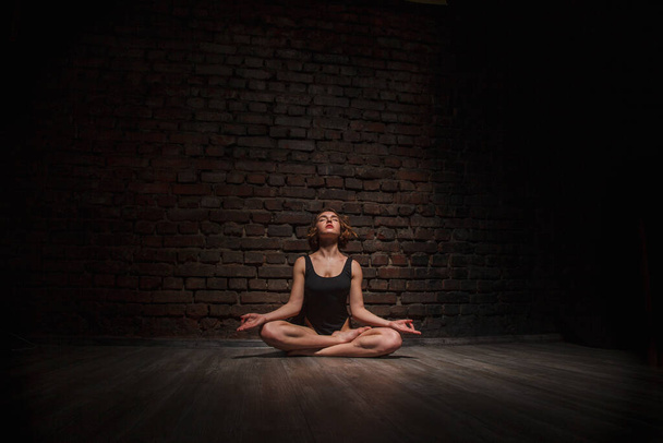 Girl in black swimsuit does yoga against the background of a brick wall - Foto, immagini