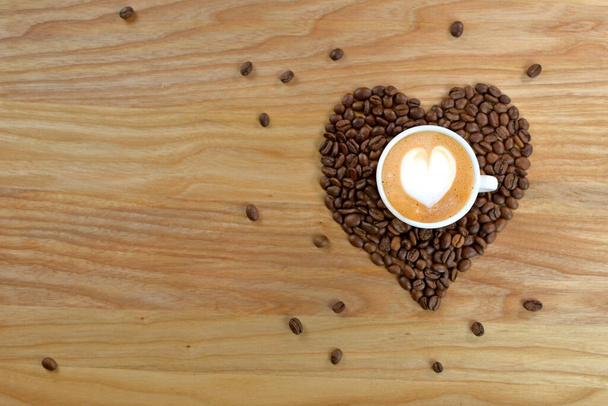 Coeur fait de grains de café, avec une tasse sur un fond en bois. Une tasse de café sur une table en bois
. - Photo, image