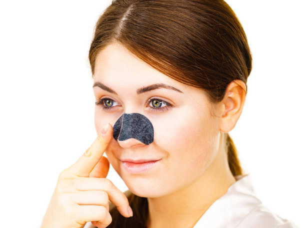 Femme appliquant des bandes claires sur le nez, à l'aide d'un masque textile nettoyant les pores, sur blanc. Fille prenant soin du teint de la peau. Soins de beauté. Soins de la peau. - Photo, image